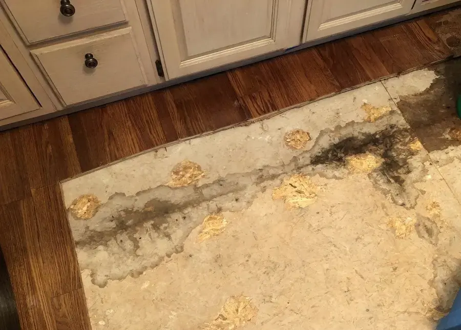 Water-stained subfloor exposed in front of kitchen cabinets after wet flooring came up